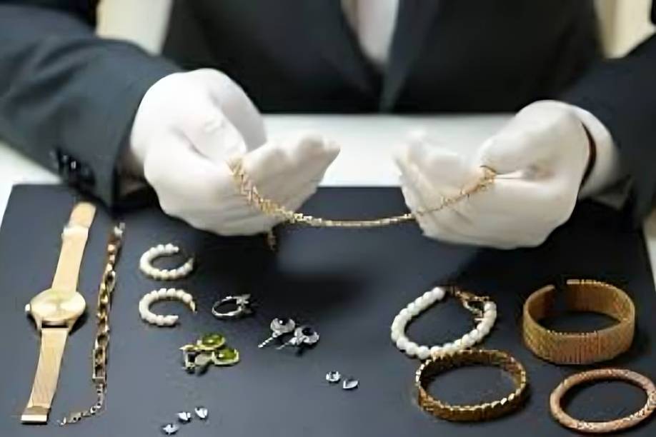 Gloved hands inspecting assorted gold and pearl jewelry